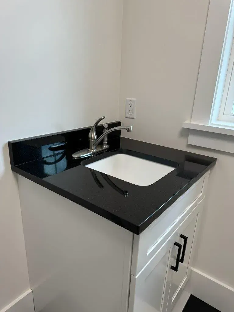 Black bathroom vanity with white sink and chrome faucet beside a window.