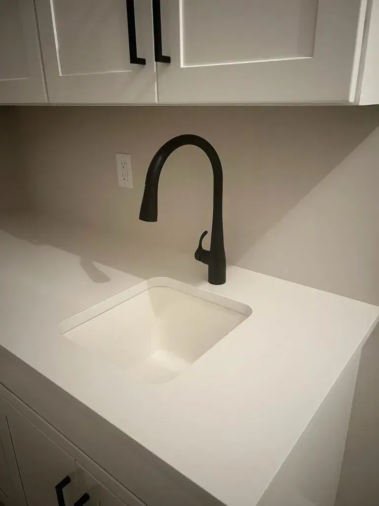 White kitchen counter with a square sink and matte black faucet under cabinets.