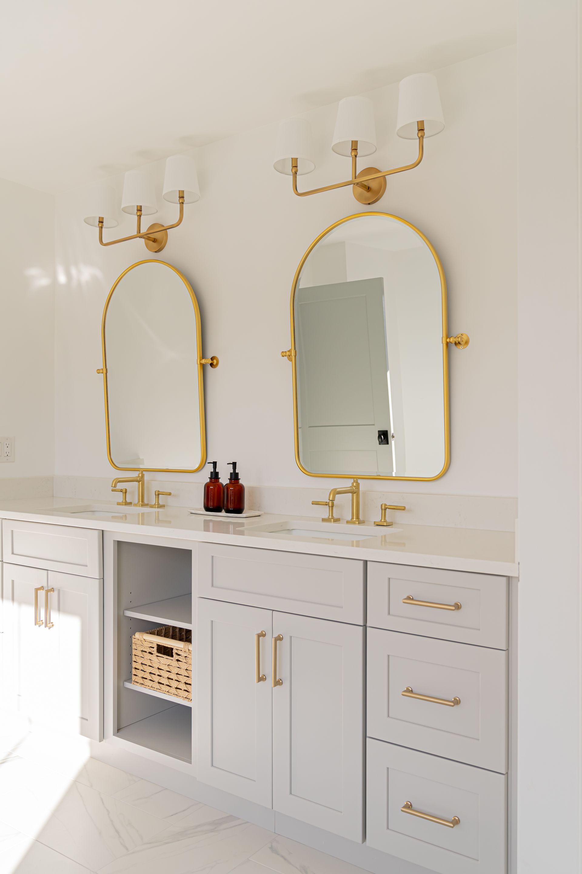 Bright bathroom vanity with two gold-framed mirrors, white and gray cabinetry, and gold wall sconces