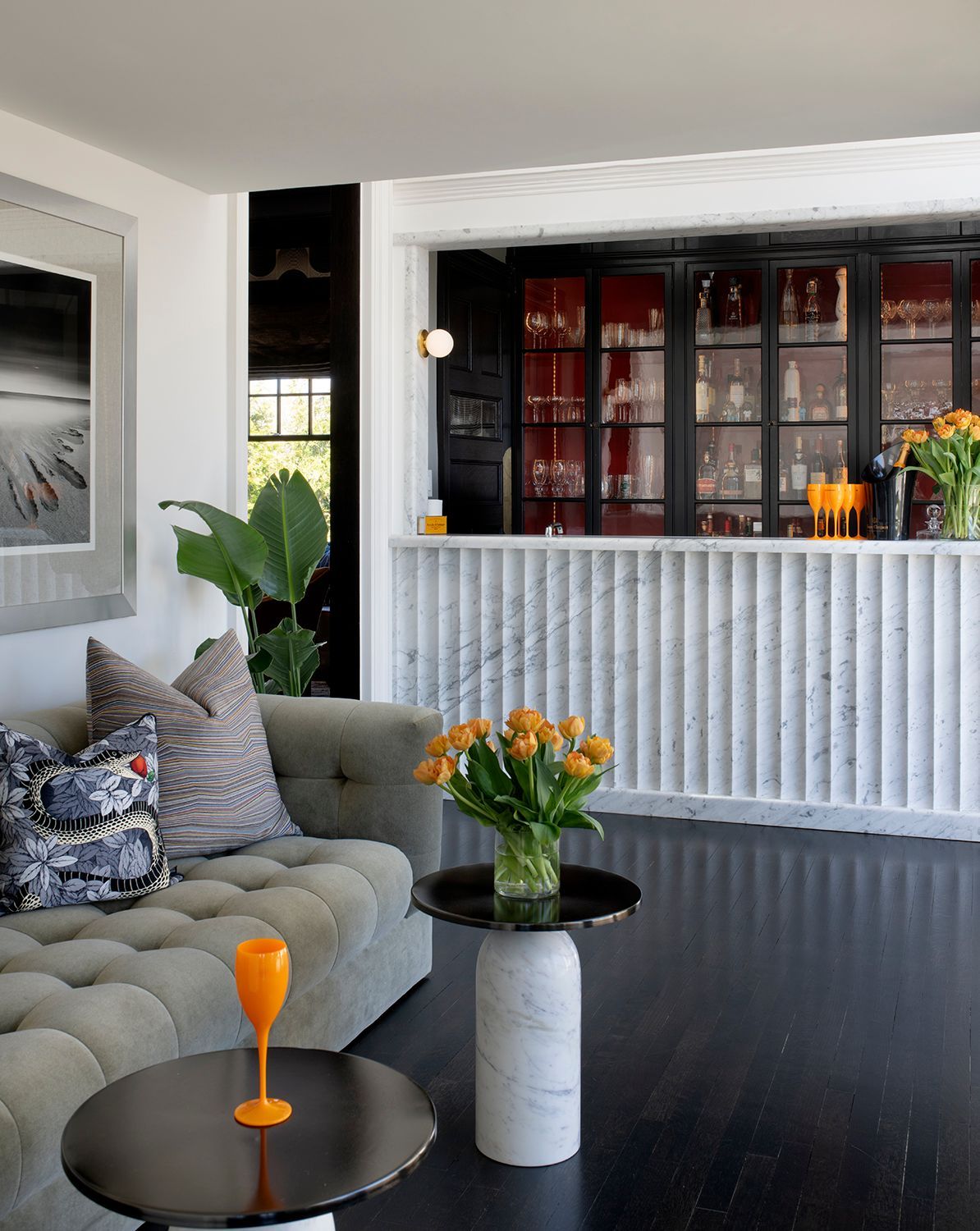 Modern living room with gray sofa, black floor, white bar, and flowers in vases