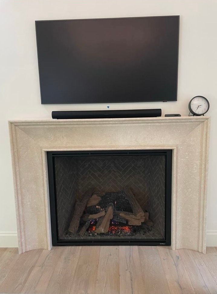Living room fireplace with mounted TV, soundbar, and clock on the mantel
