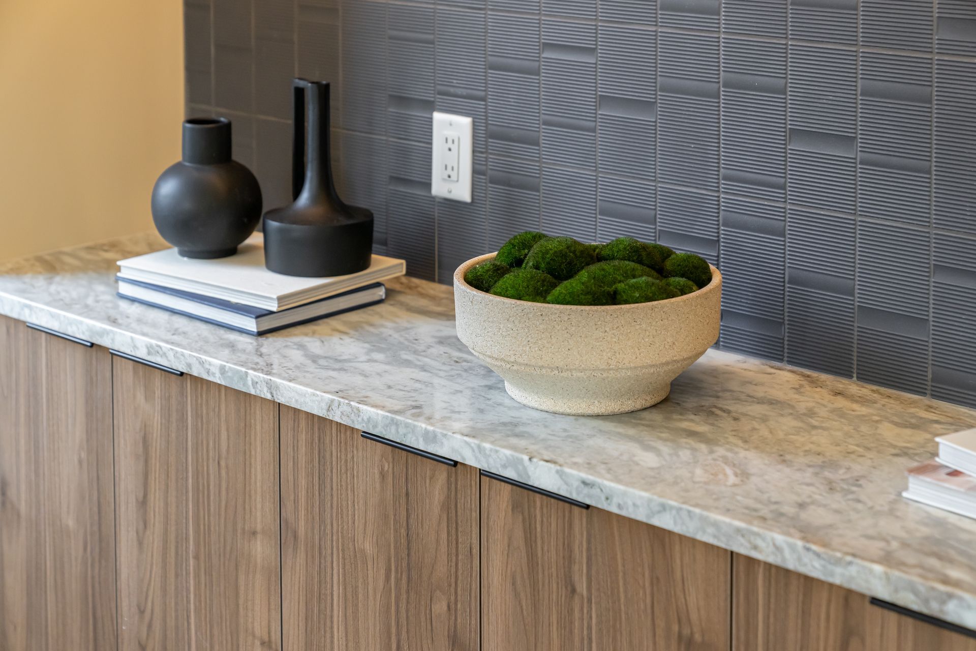 Decorative countertop with vases, books, and a moss-filled bowl against a textured gray wall.