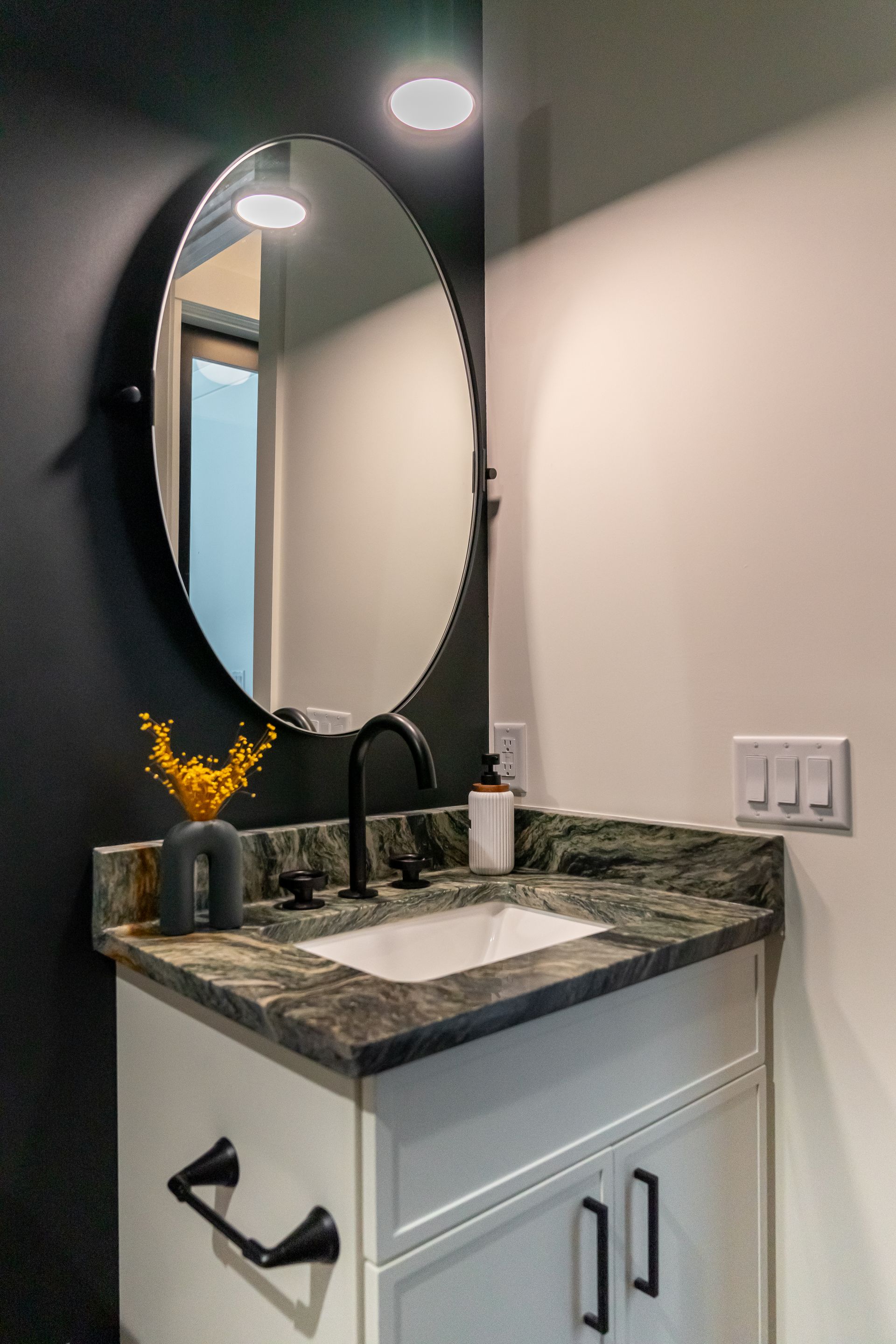 Small bathroom vanity with round mirror, granite countertop, wall sconce, and white cabinet doors