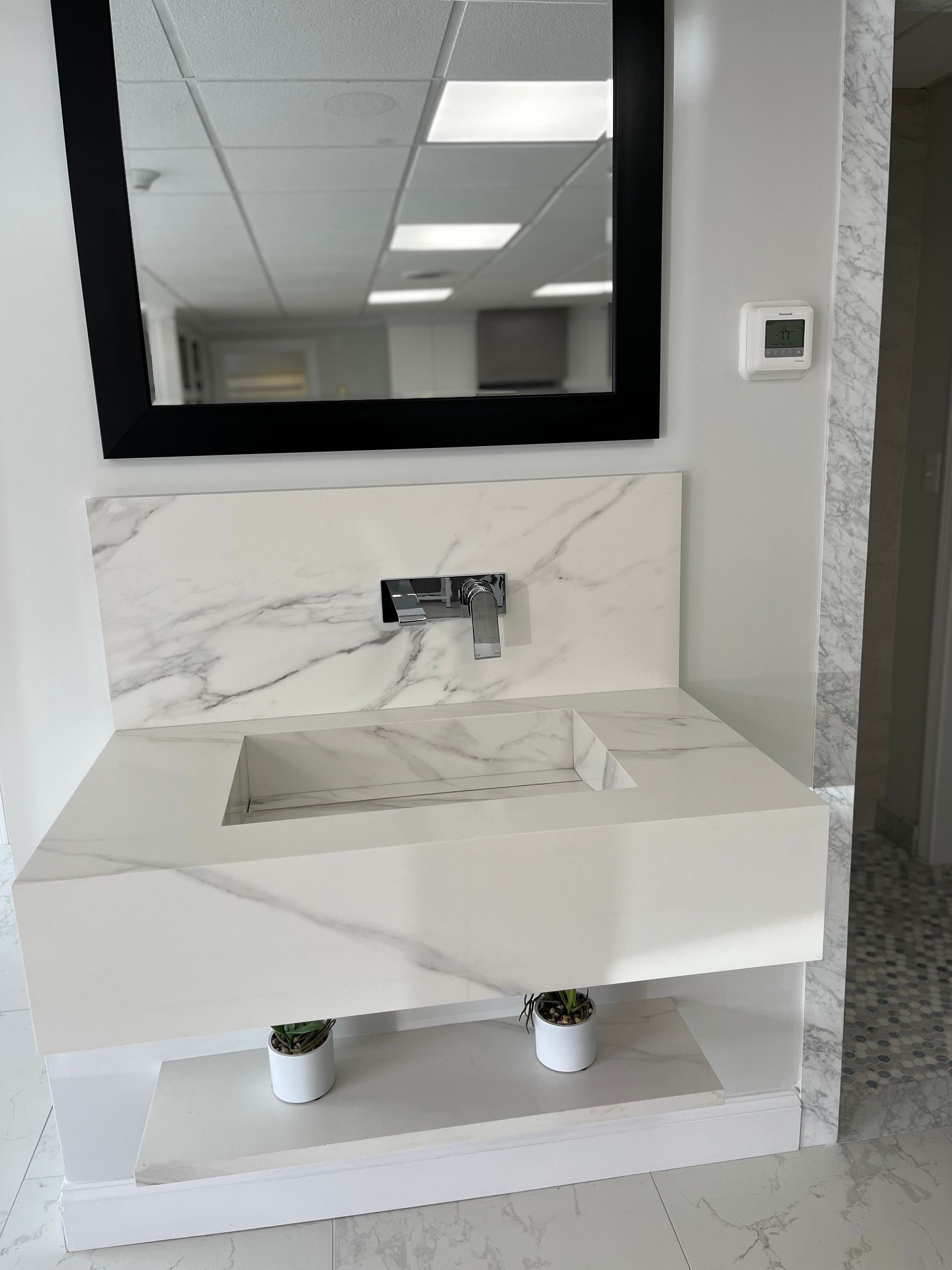 Modern white bathroom vanity with marble backsplash, black-framed mirror, and small sink in a bright room