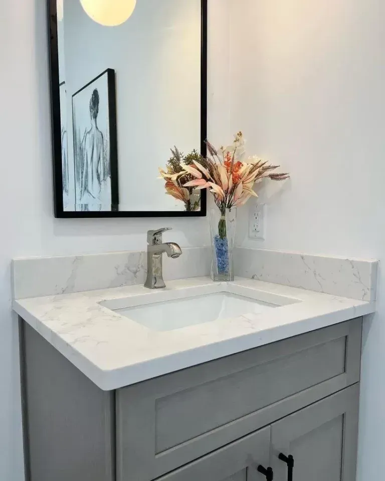 Modern bathroom vanity with white sink, gray cabinet, mirror, and vase of dried flowers