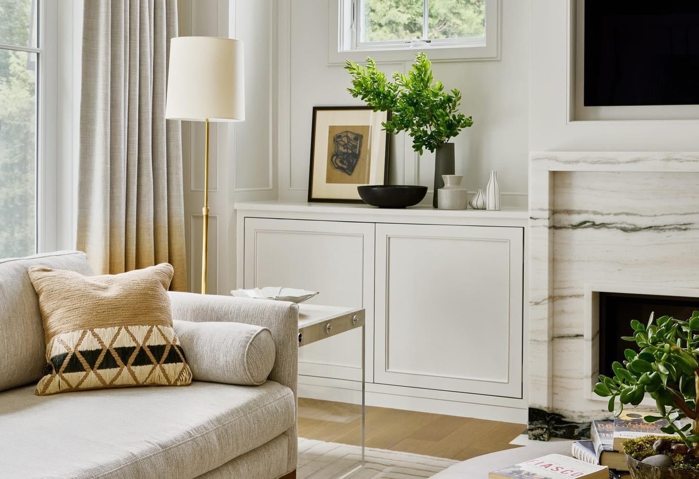Bright living room with beige sofa, floor lamp, white cabinet, and fireplace with green plants
