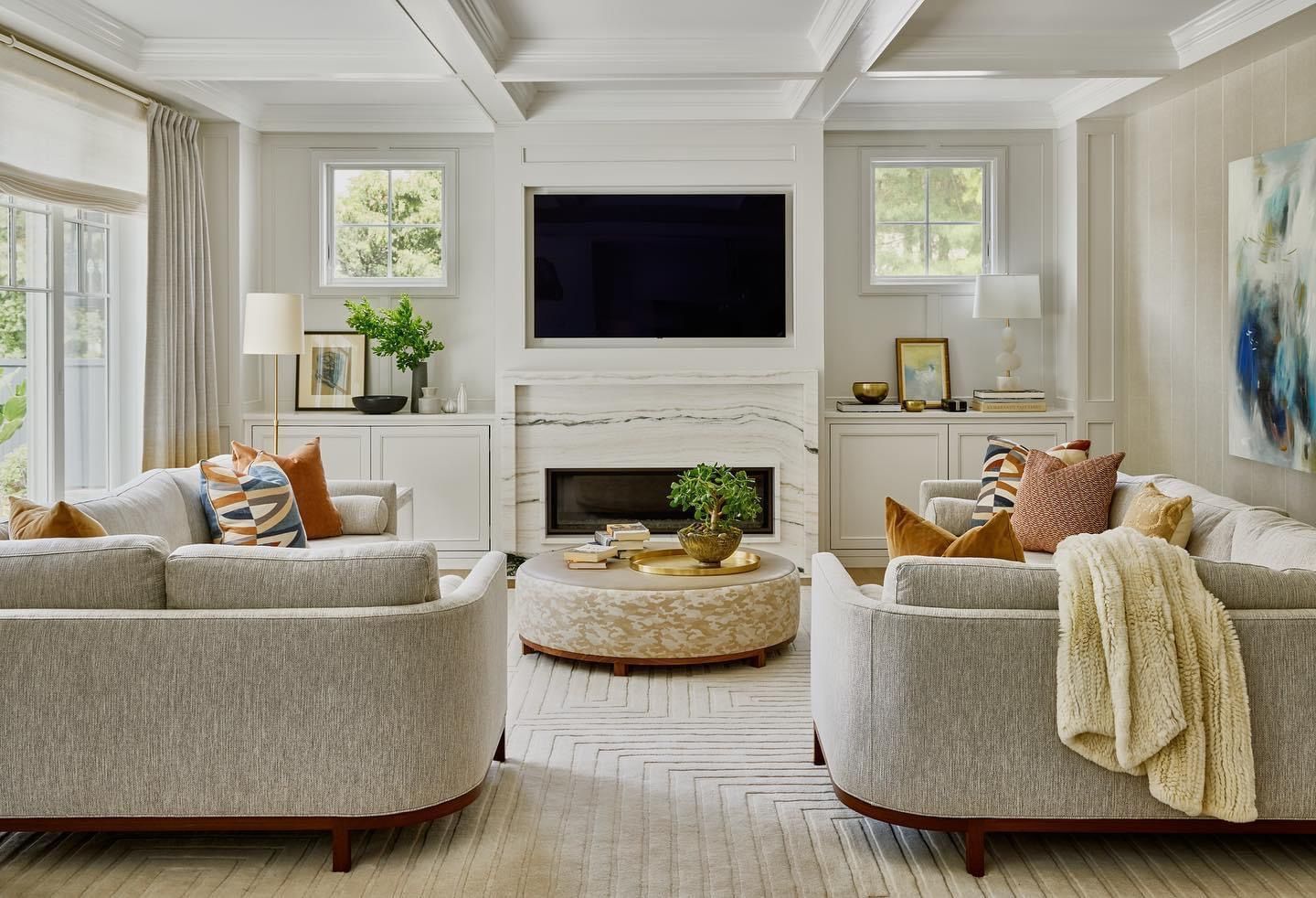 Bright living room with white sofas, a wall-mounted TV, and a round coffee table centered on a light rug.