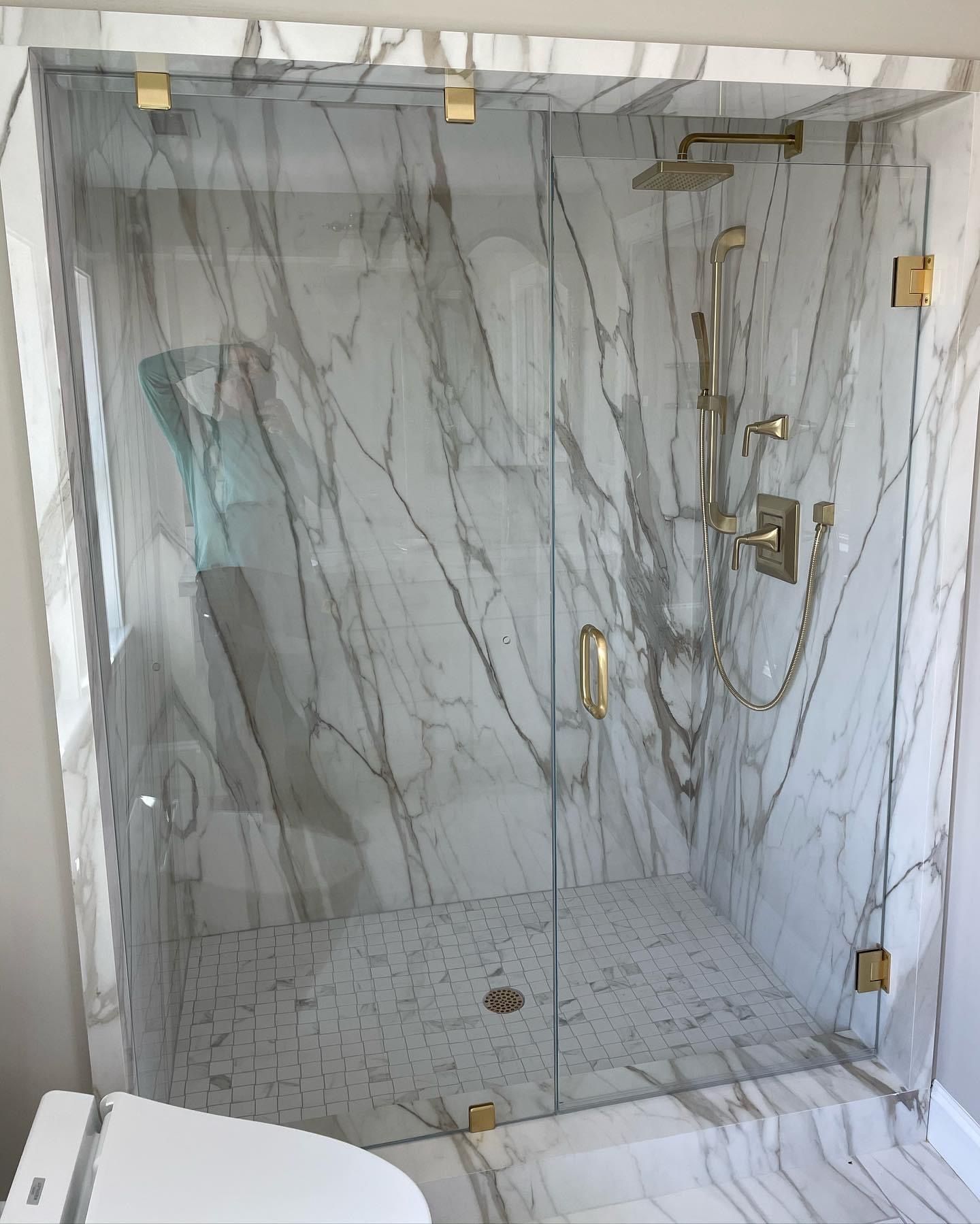 Marble-tiled glass shower with brass fixtures and a built-in bench