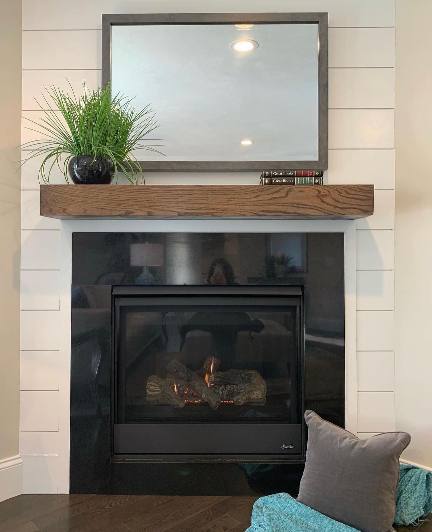 Modern fireplace with white tile surround, dark insert, wooden mantel, mirror, and decorative plant and pillows