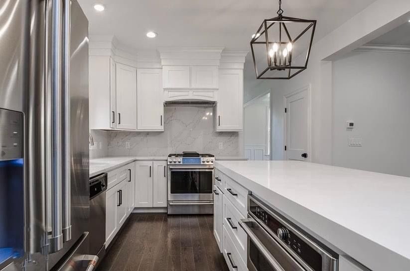 Modern white kitchen with stainless steel appliances, dark wood floors, and a large island with pendant light