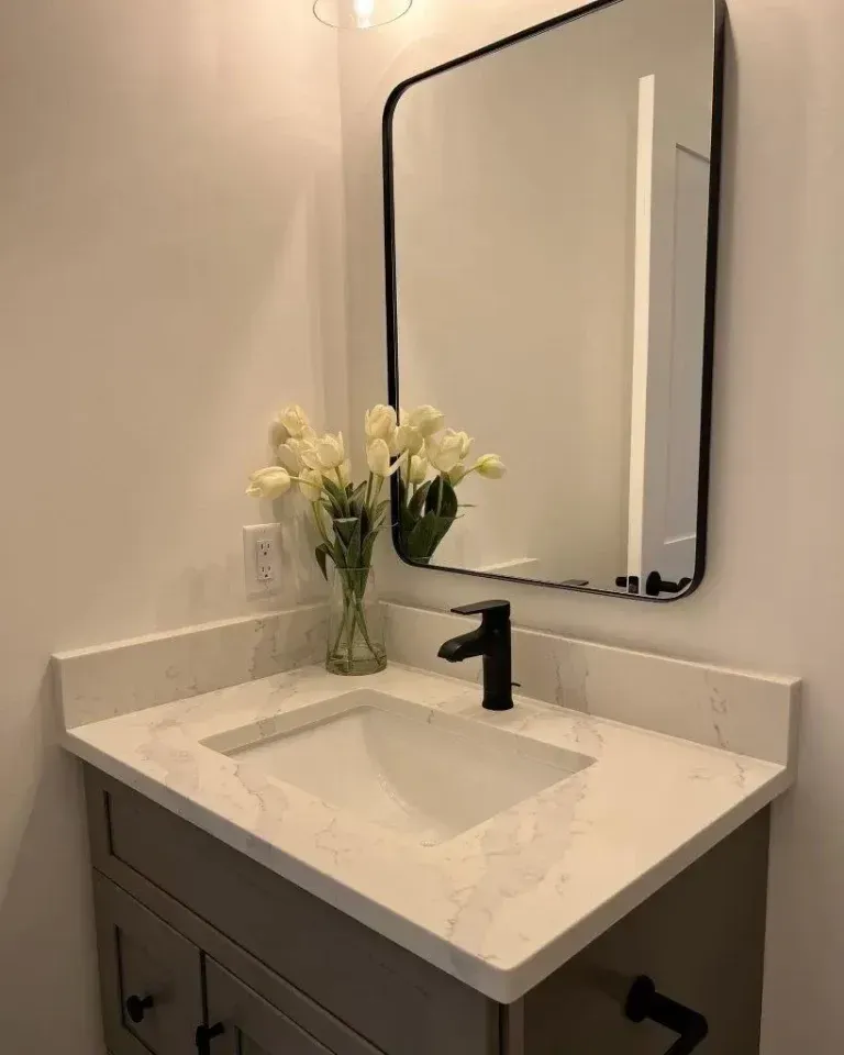 White bathroom vanity with black faucet, large mirror, and vase of white flowers