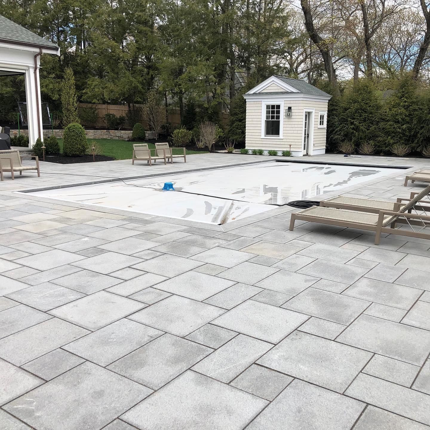 Backyard patio with a covered pool, white shed, and stone pavers beside lounge chairs.