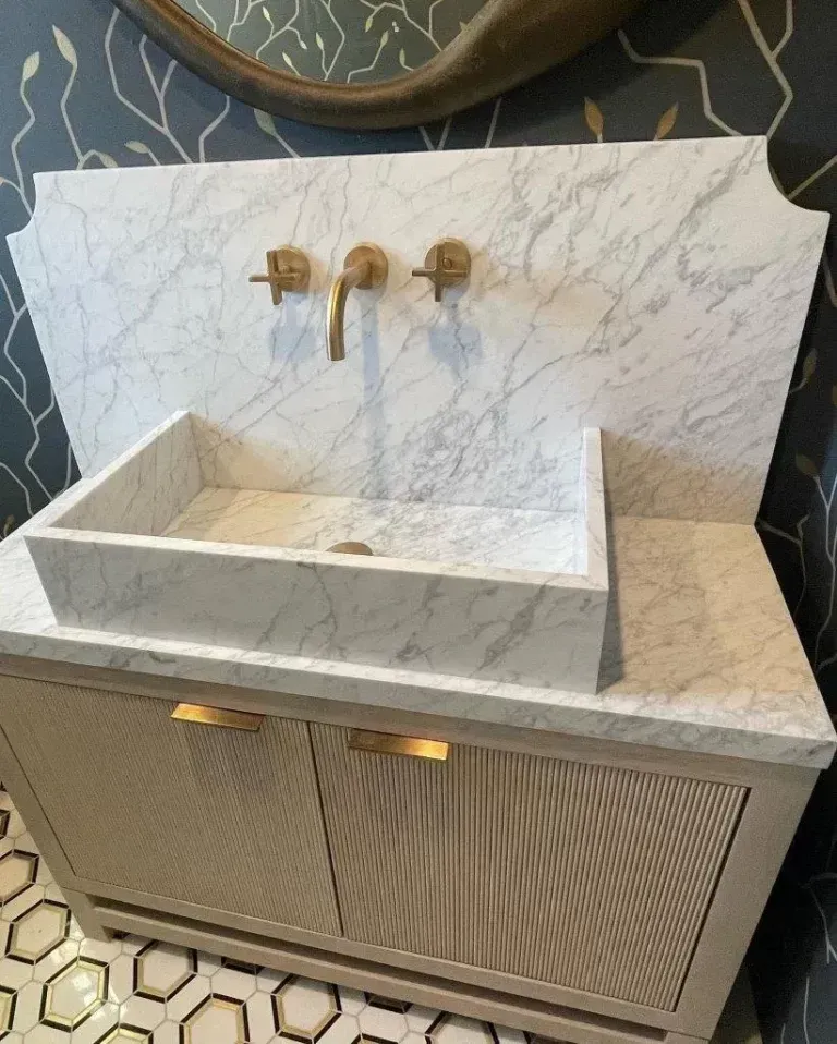 Marble sink vanity with gold faucets and under-cabinet lights in a modern bathroom