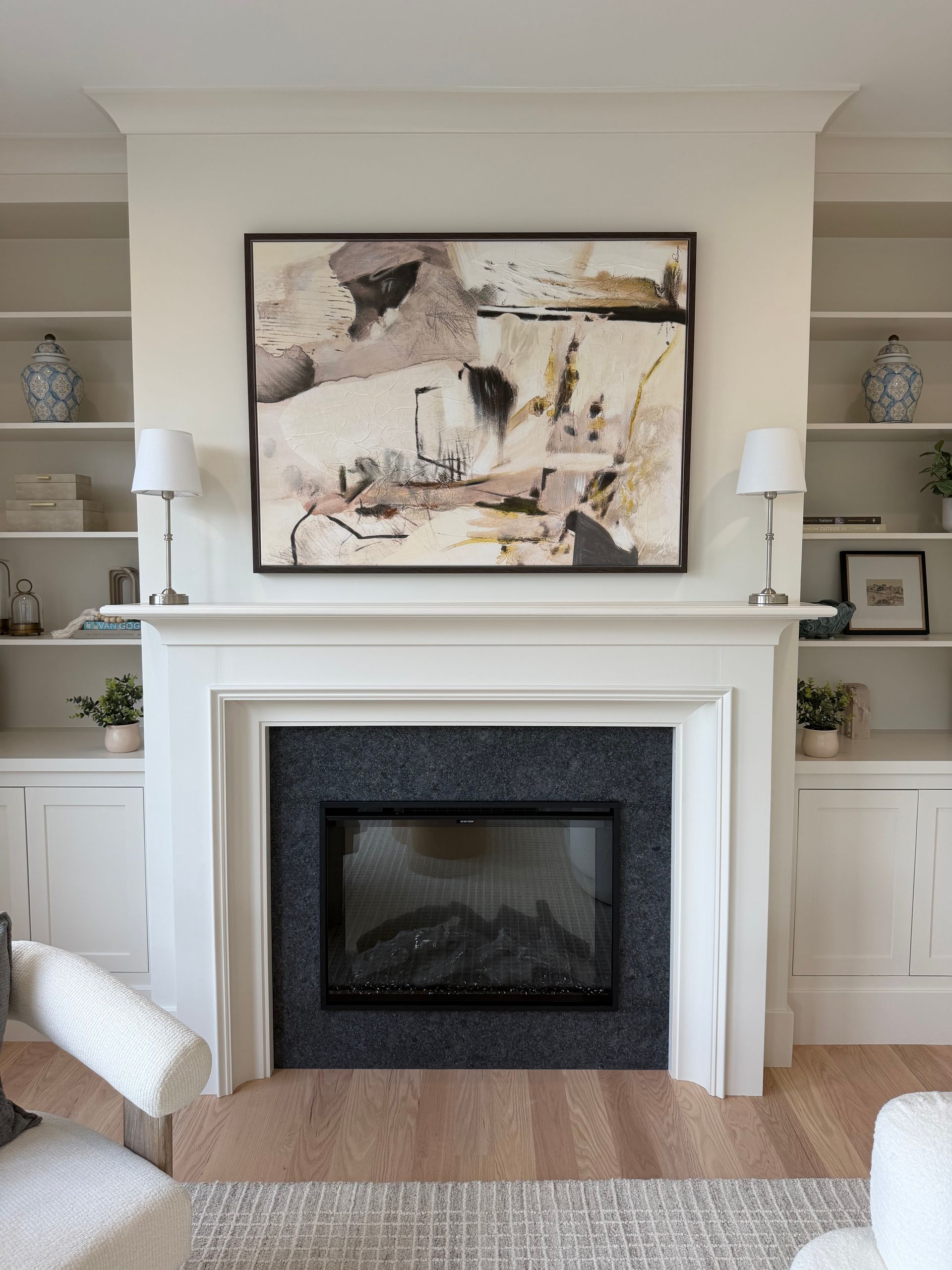 Living room fireplace with abstract art, white mantel, built-in shelves, and neutral decor