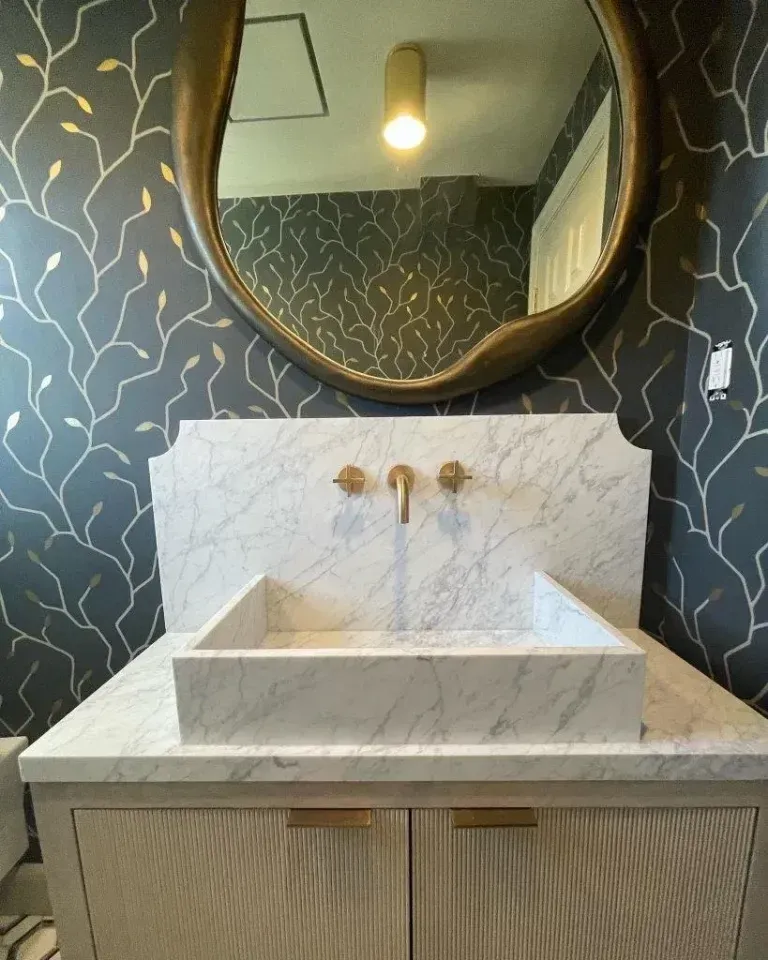 Modern bathroom vanity with round mirror, marble sink, and dark patterned wallpaper.
