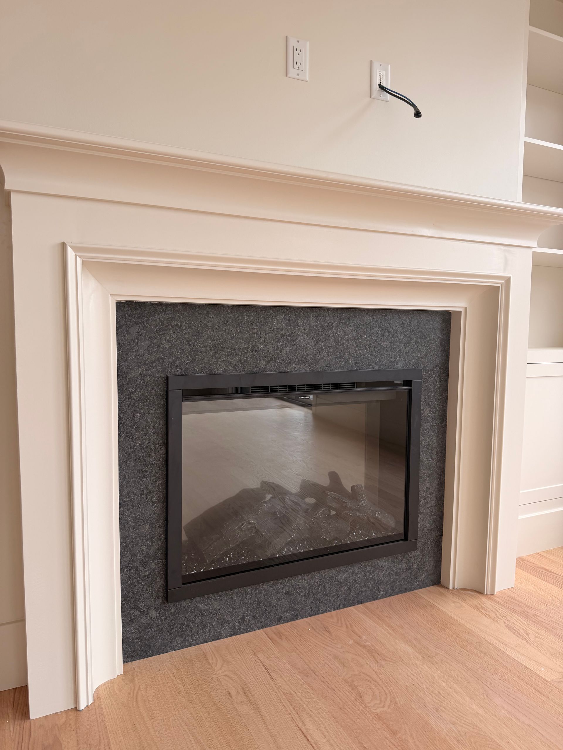 White fireplace with dark stone surround in a beige room, with a light wood floor.