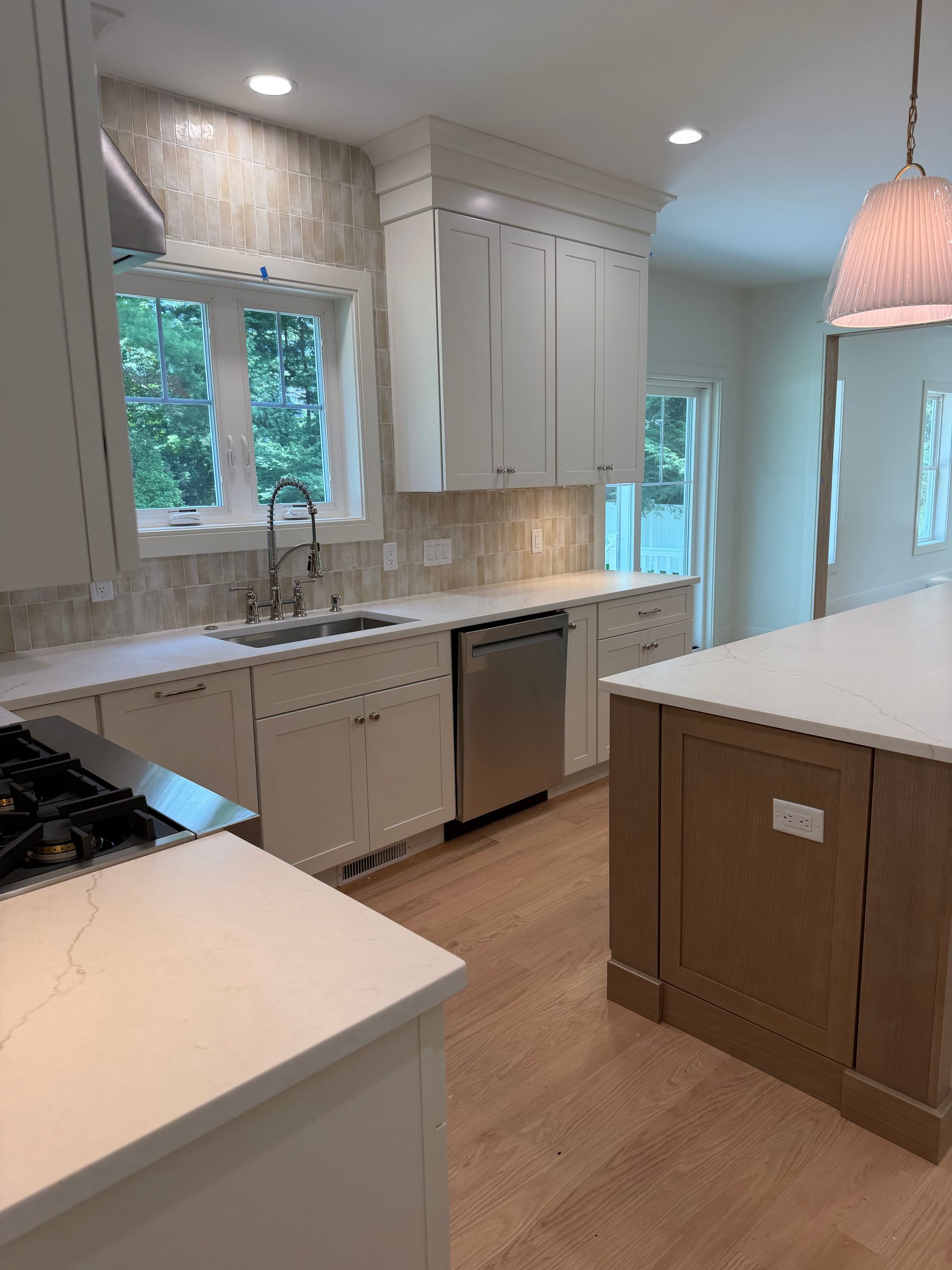 Bright modern kitchen with white cabinets, marble counters, and large windows overlooking trees