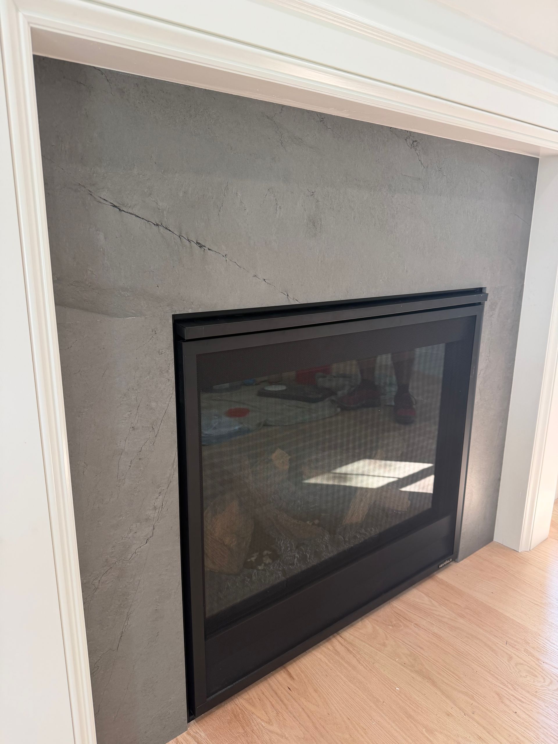 Black glass-front fireplace with gray stone surround and white mantel in a room with light wood flooring