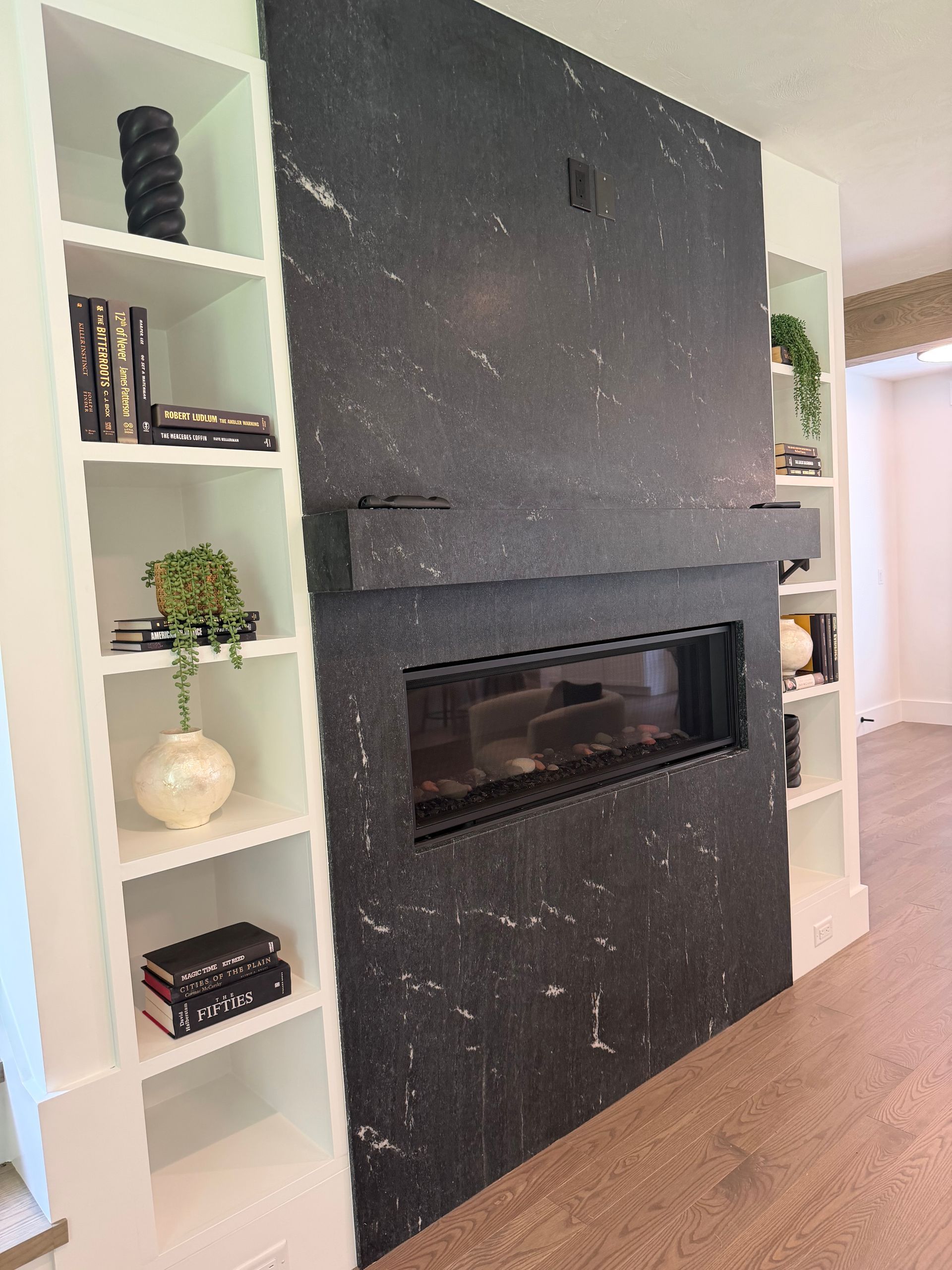 Modern living room wall with a large black fireplace surround and white built-in shelves on both sides.
