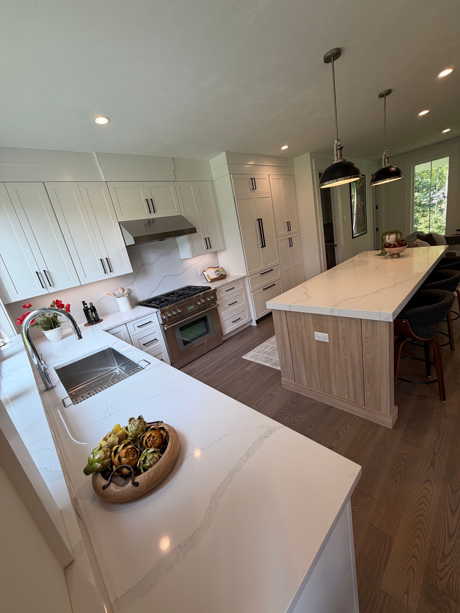 Bright modern kitchen with white cabinets, large island, pendant lights, and wood flooring
