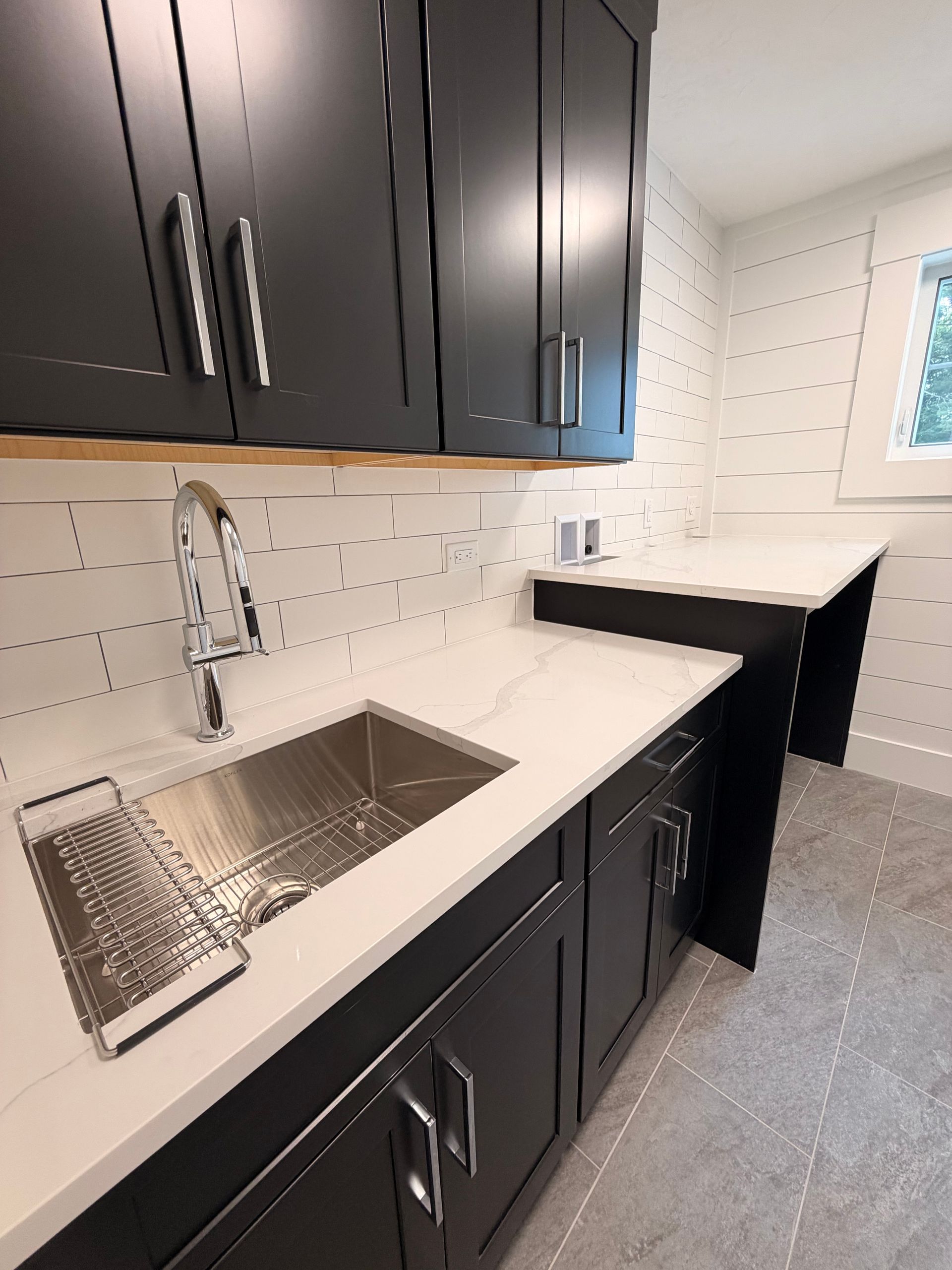 Modern kitchen with dark cabinets, white countertops, stainless sink, and patterned white tile walls.