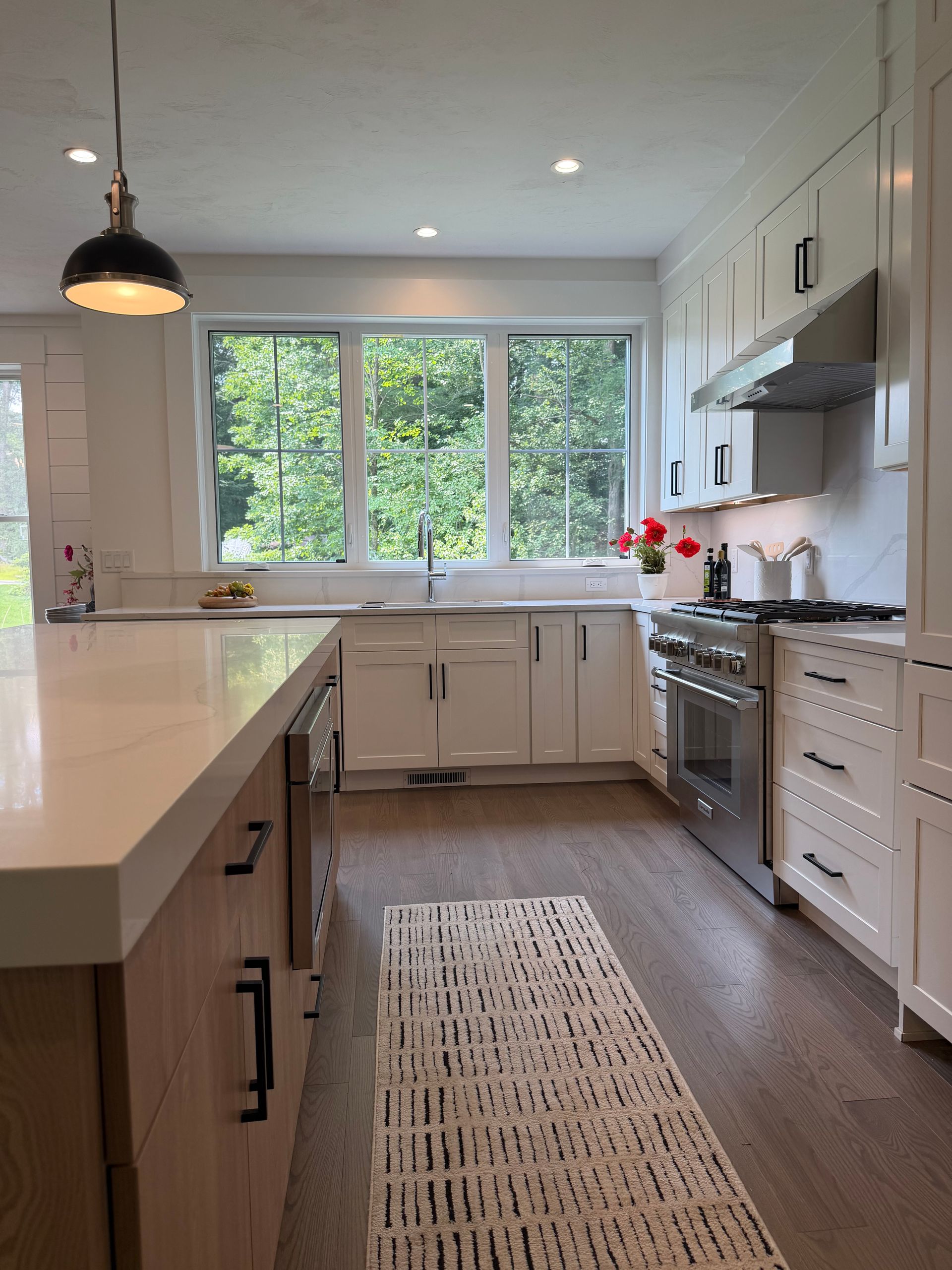 Bright modern kitchen with white cabinets, island, stainless stove, and large window over a rug