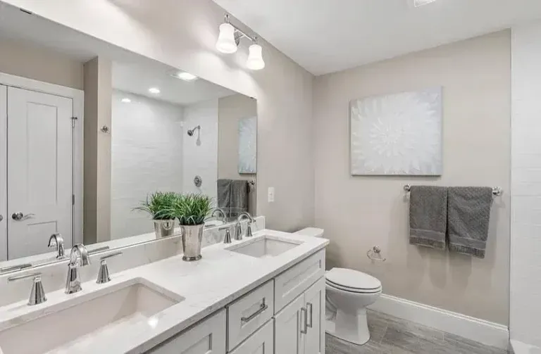 Bright modern bathroom with double sink vanity, mirror, toilet, towel rack, and white/gray decor