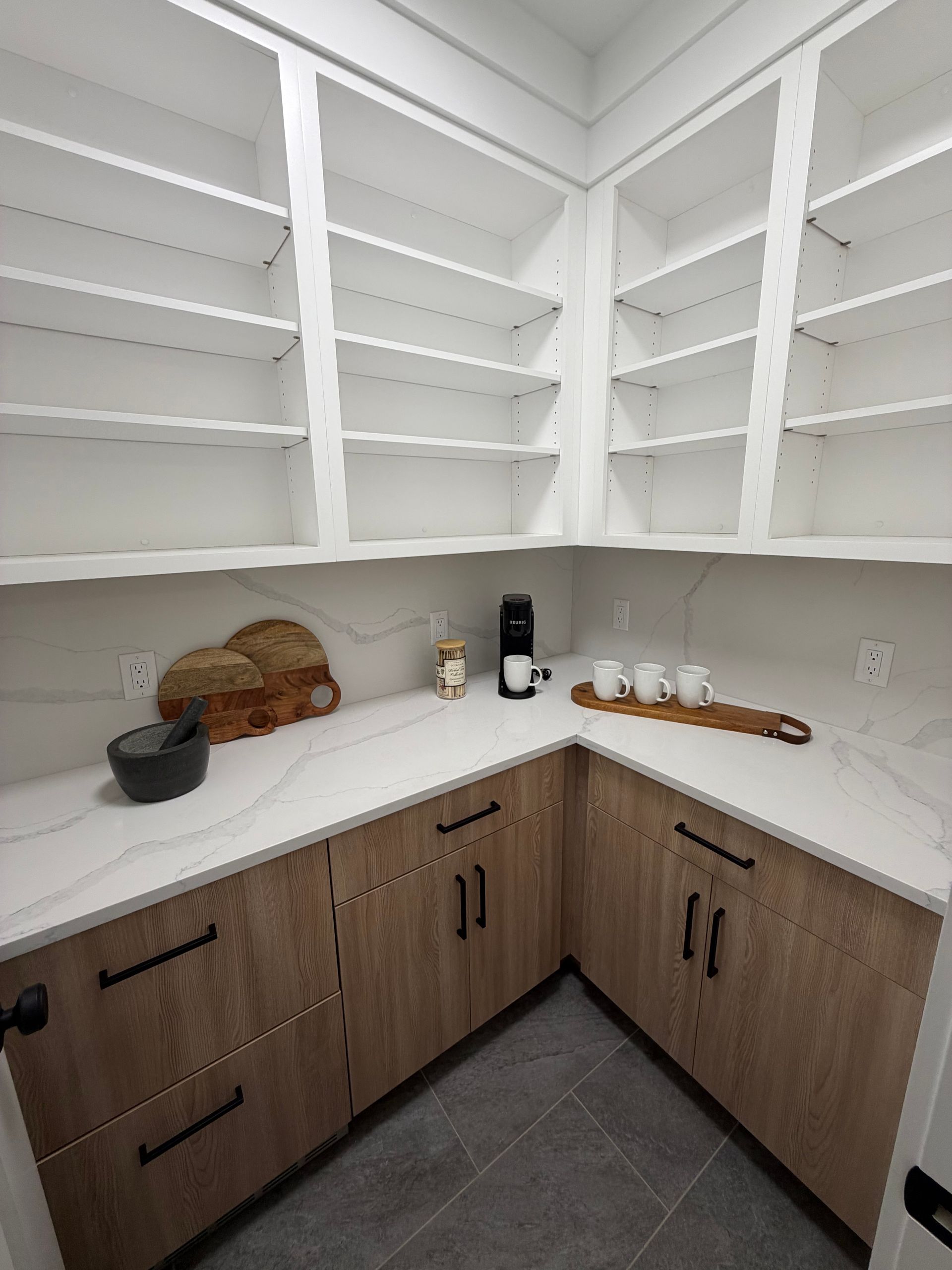 Corner kitchen pantry with white shelves, wood lower cabinets, and a few items on the countertop.