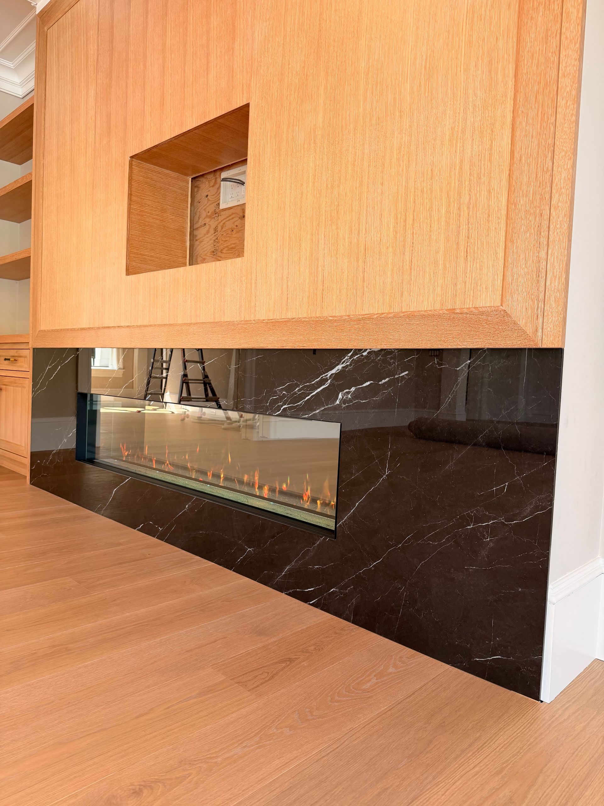 Wooden cabinet with a small rectangular cutout above a black marble fireplace opening