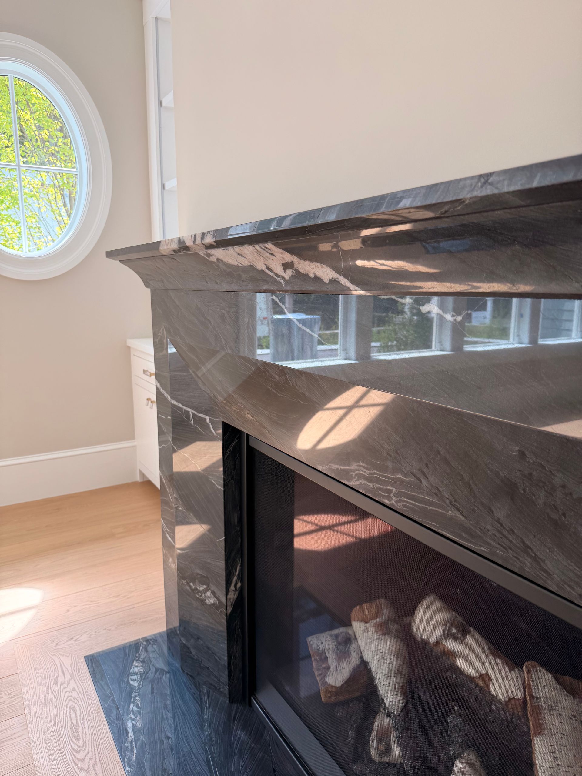 Black marble fireplace mantel in a bright room with sunlight and a round window.