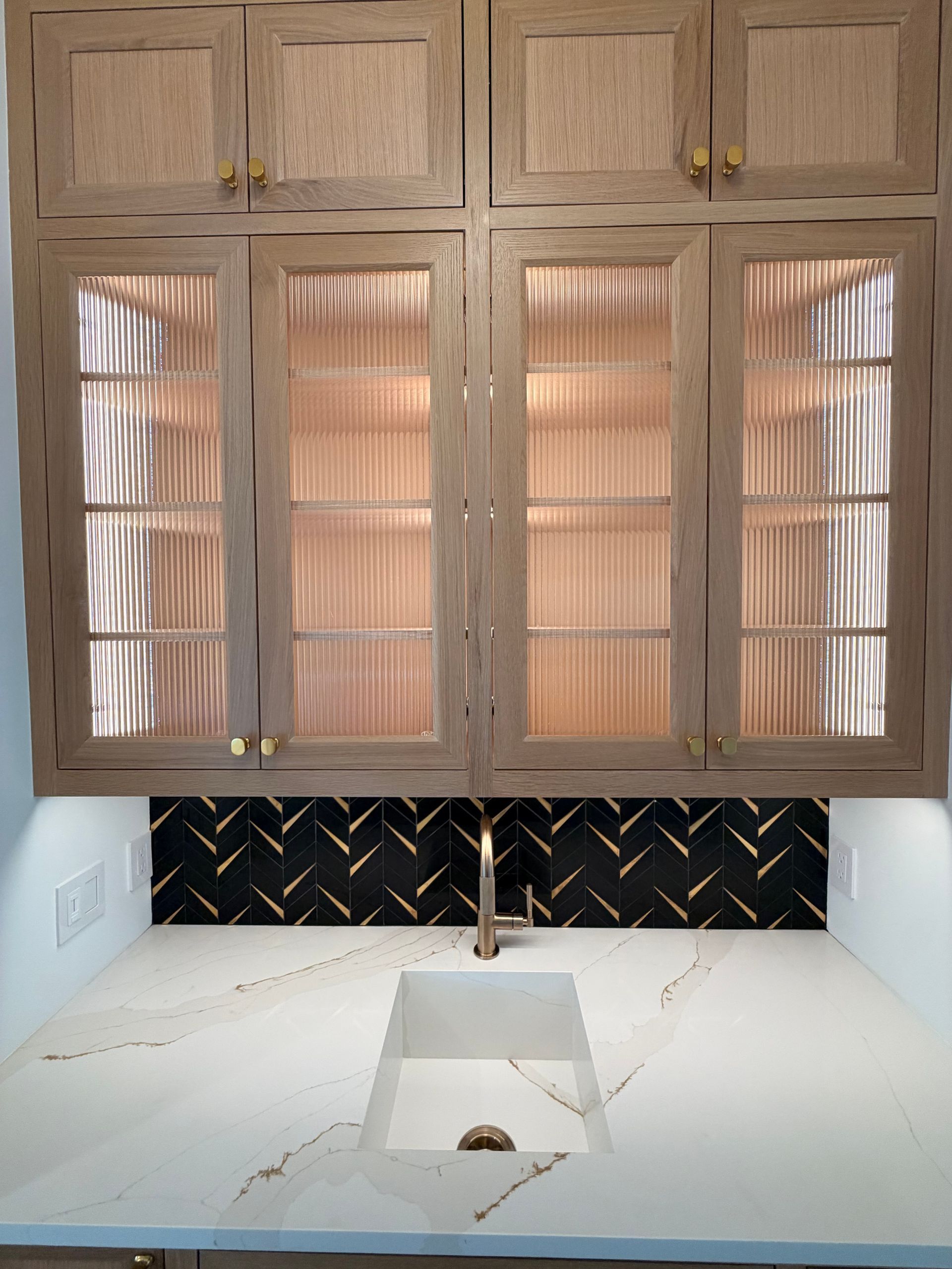 Modern kitchen sink with beige cabinets, black backsplash, and white marble countertop