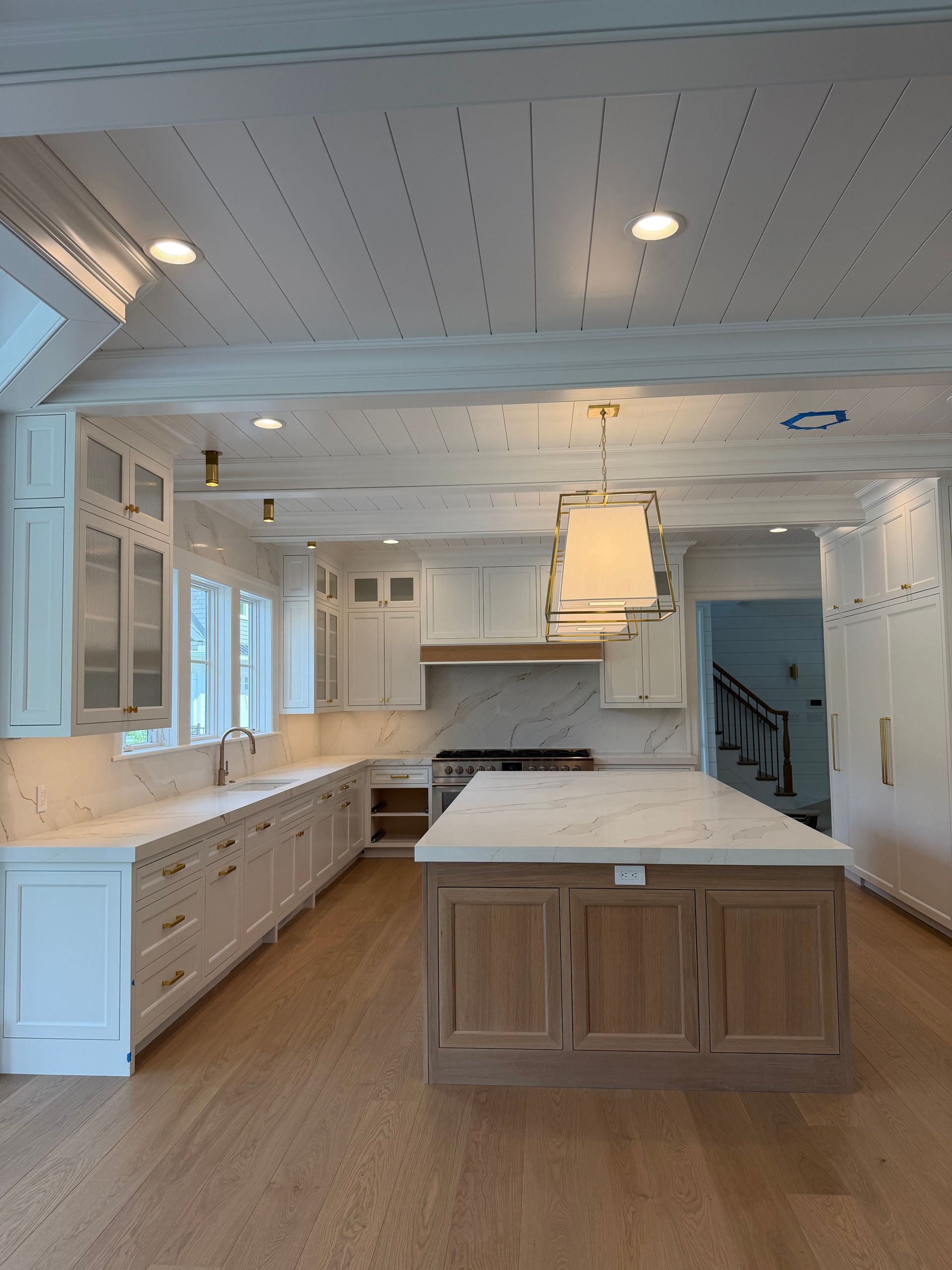 Bright white farmhouse kitchen with wood island, marble counters, and pendant light beneath a paneled ceiling