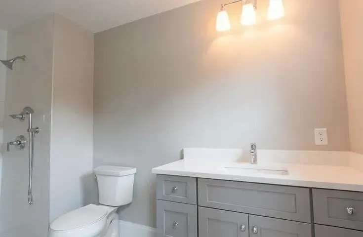 Modern bathroom with gray vanity, white countertop, toilet, and shower stall
