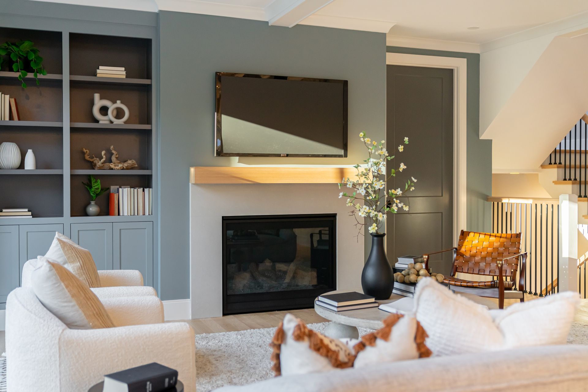 Modern living room with gray fireplace wall, mounted TV, white sofas, and built-in shelves