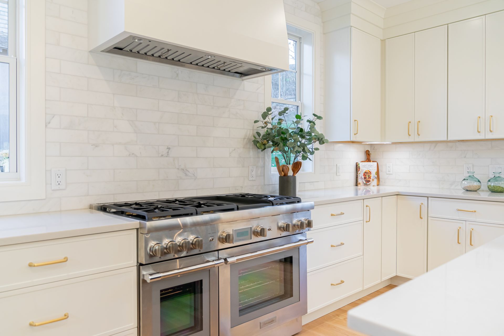 Bright white kitchen with stainless steel stove, tiled backsplash, and a vase of flowers by the window