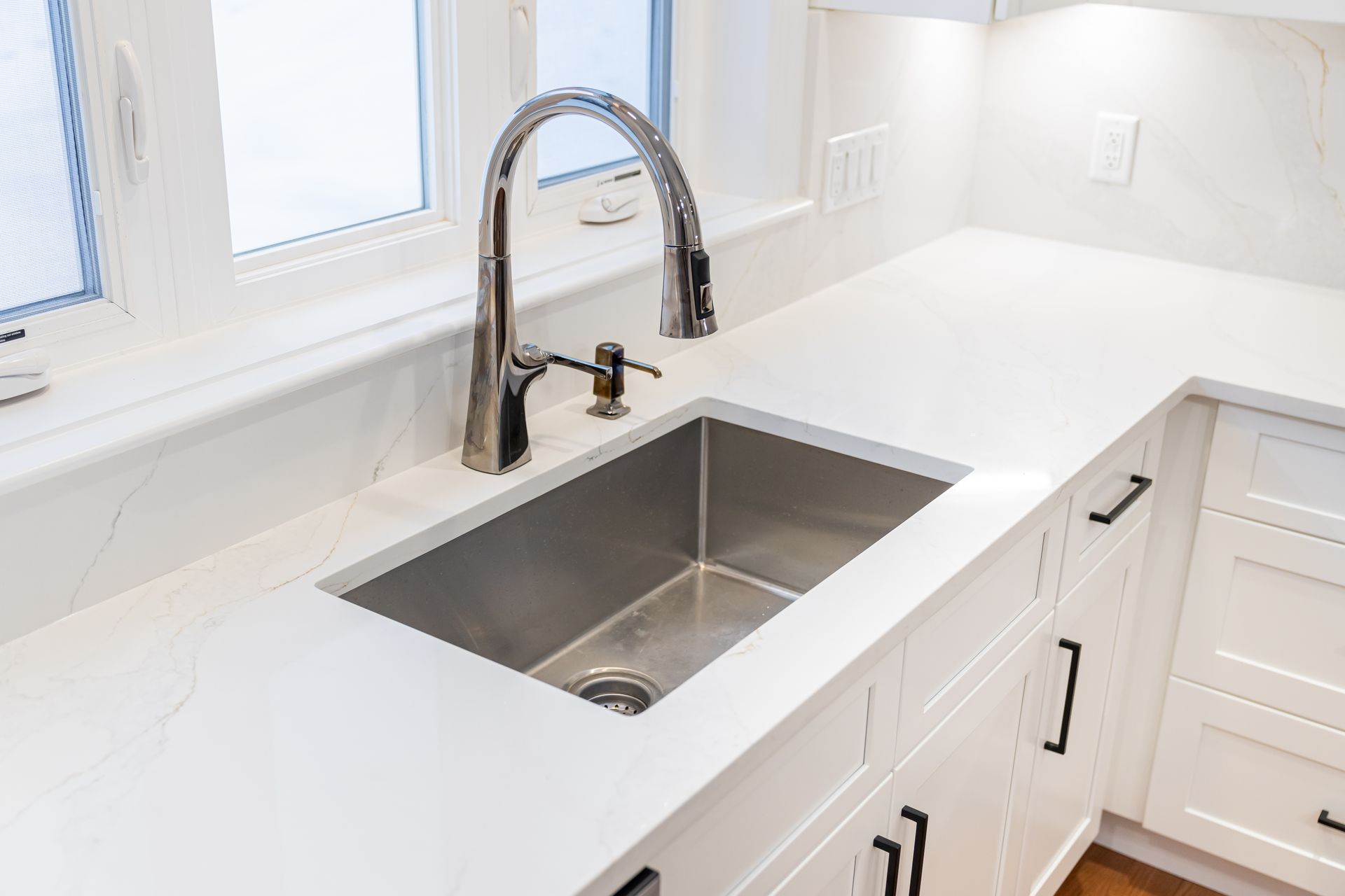 Bright white kitchen counter with a stainless steel sink and tall chrome faucet by a window