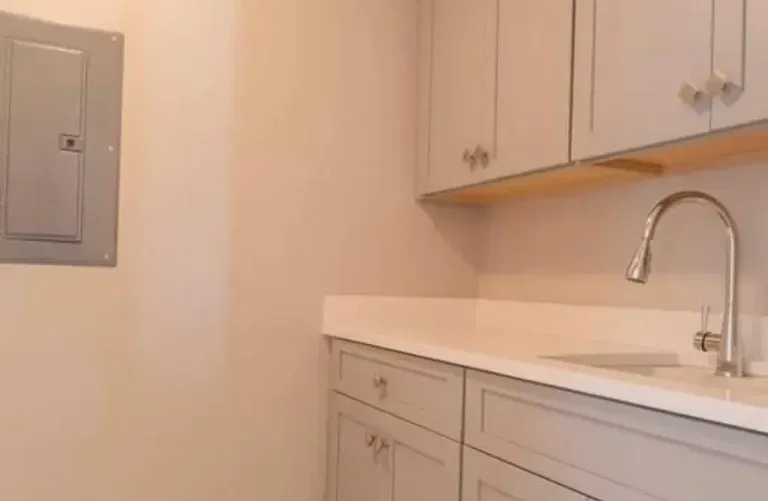 Empty beige kitchen with cabinets, countertop, sink, and a wall-mounted electrical panel