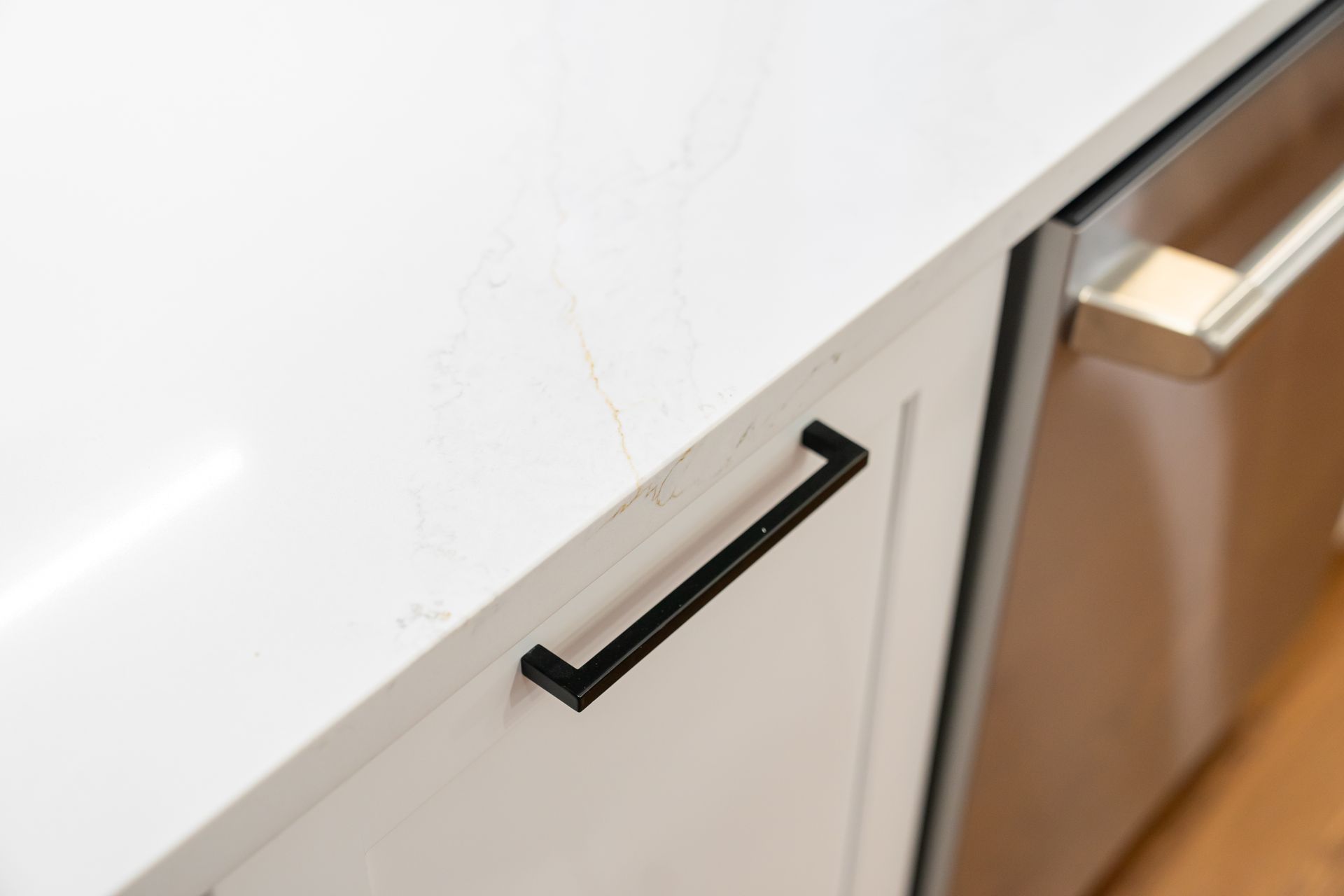 Black cabinet pull handle on a white kitchen drawer beside a wood floor