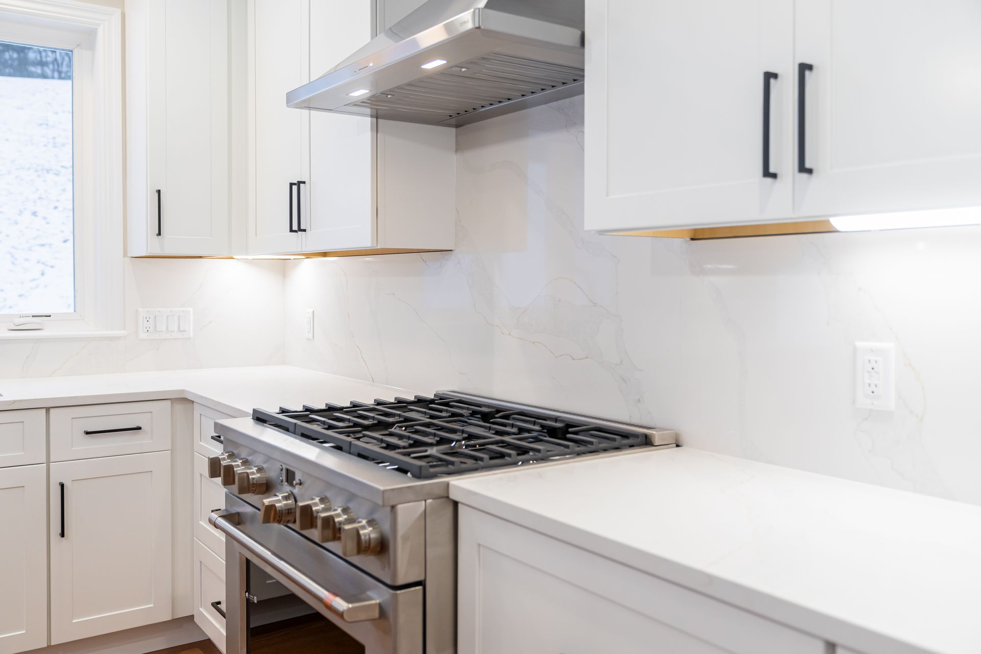 Modern white kitchen with stainless steel range, hood, and white cabinetry