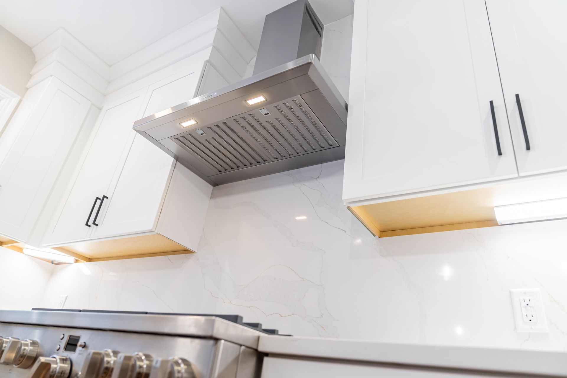 Modern white kitchen with stainless steel range hood and bright under-cabinet lighting