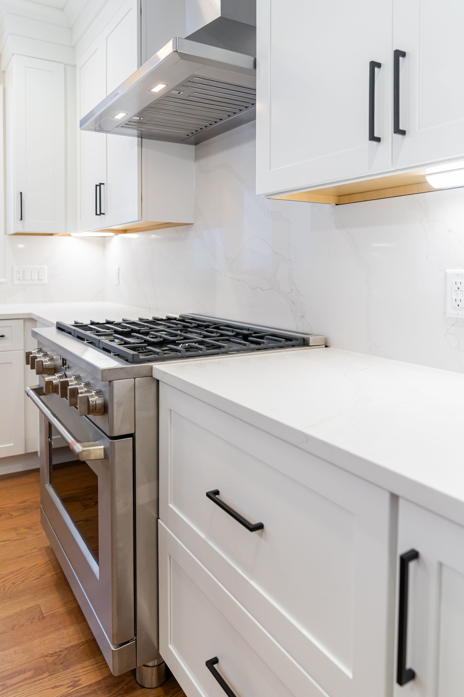 Modern white kitchen with gas stove, stainless hood, and light countertops