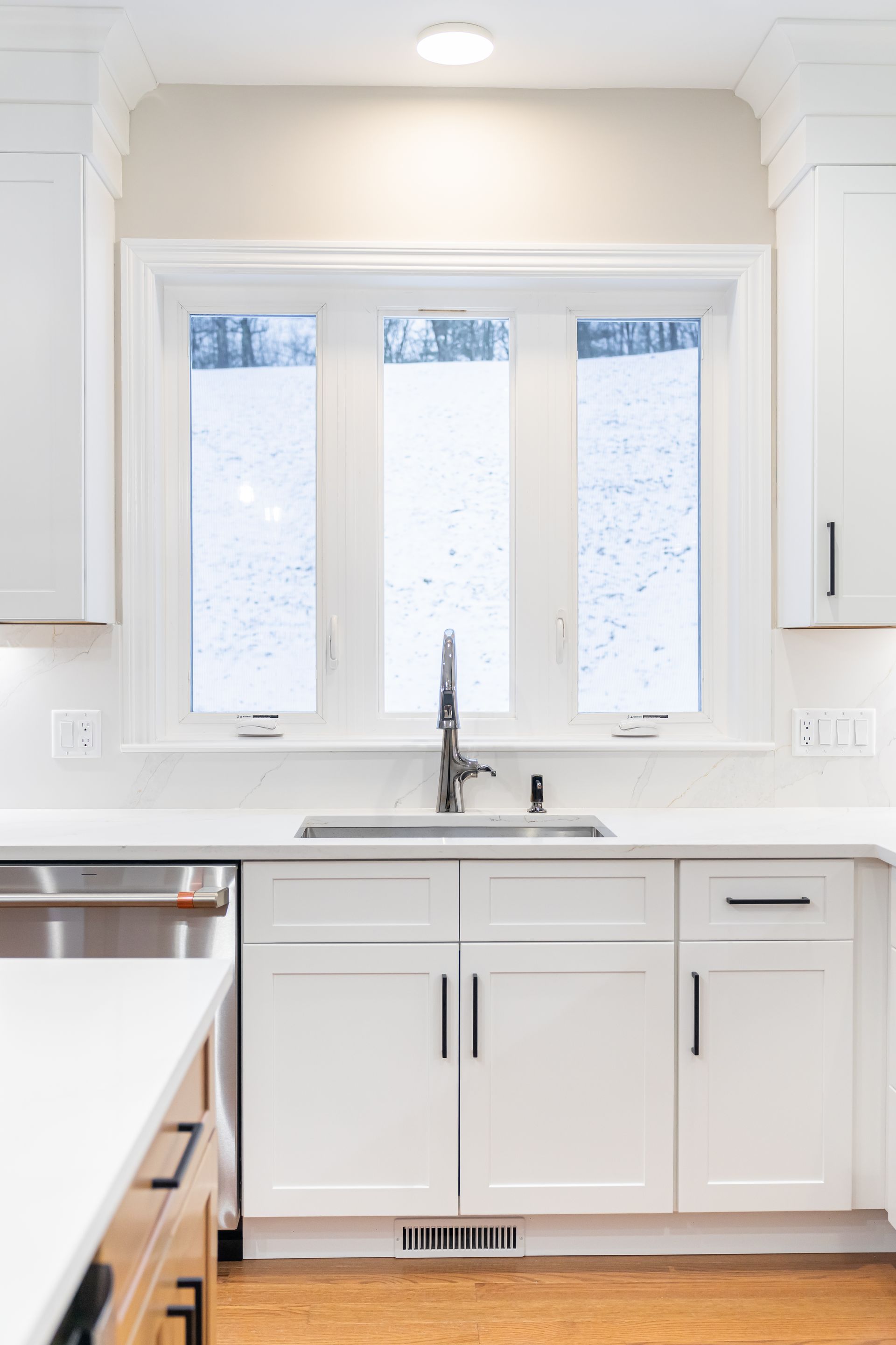 Bright white kitchen sink area with three frosted windows, stainless faucet, and white cabinets
