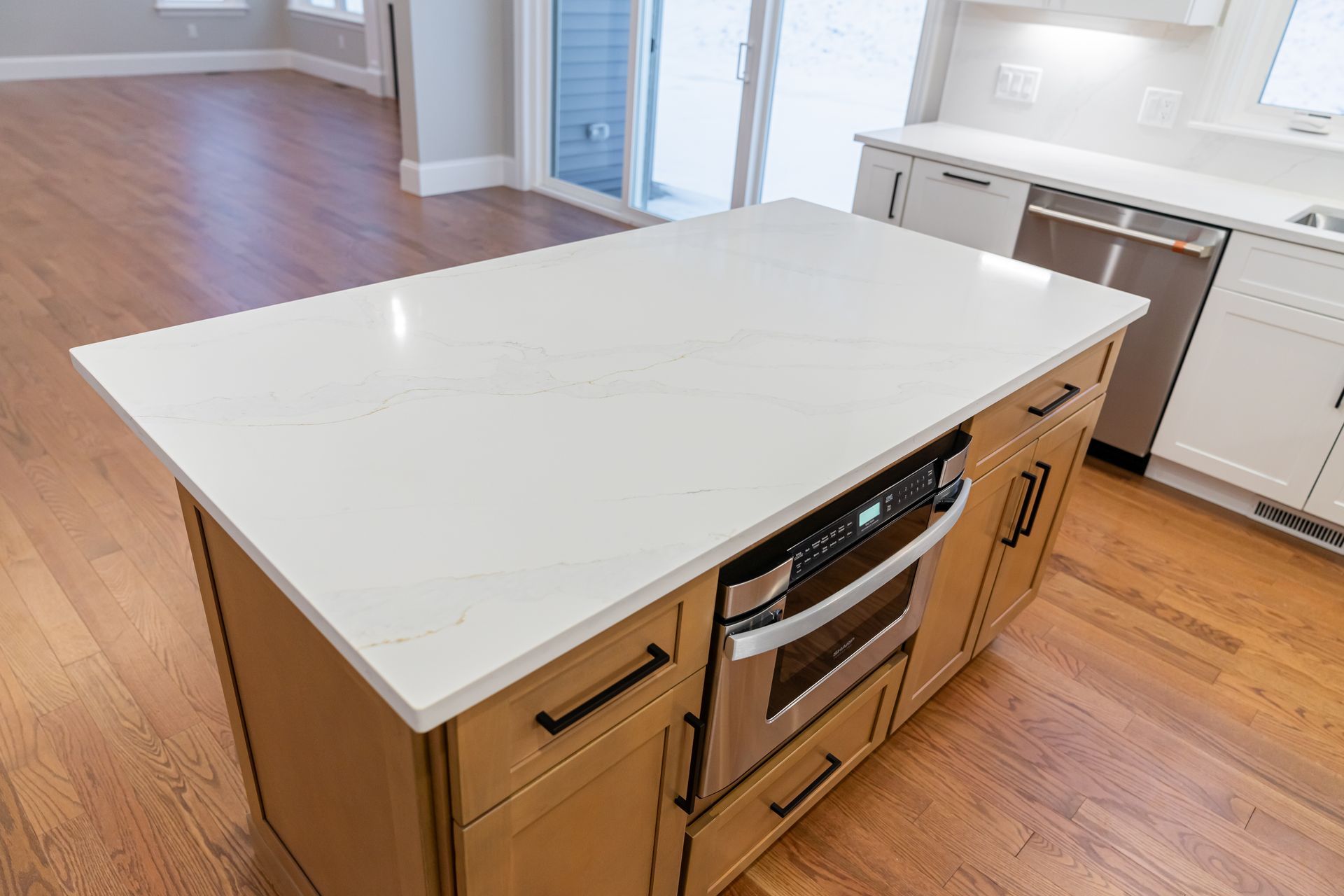 Modern kitchen island with white quartz countertop and built-in oven in a bright room