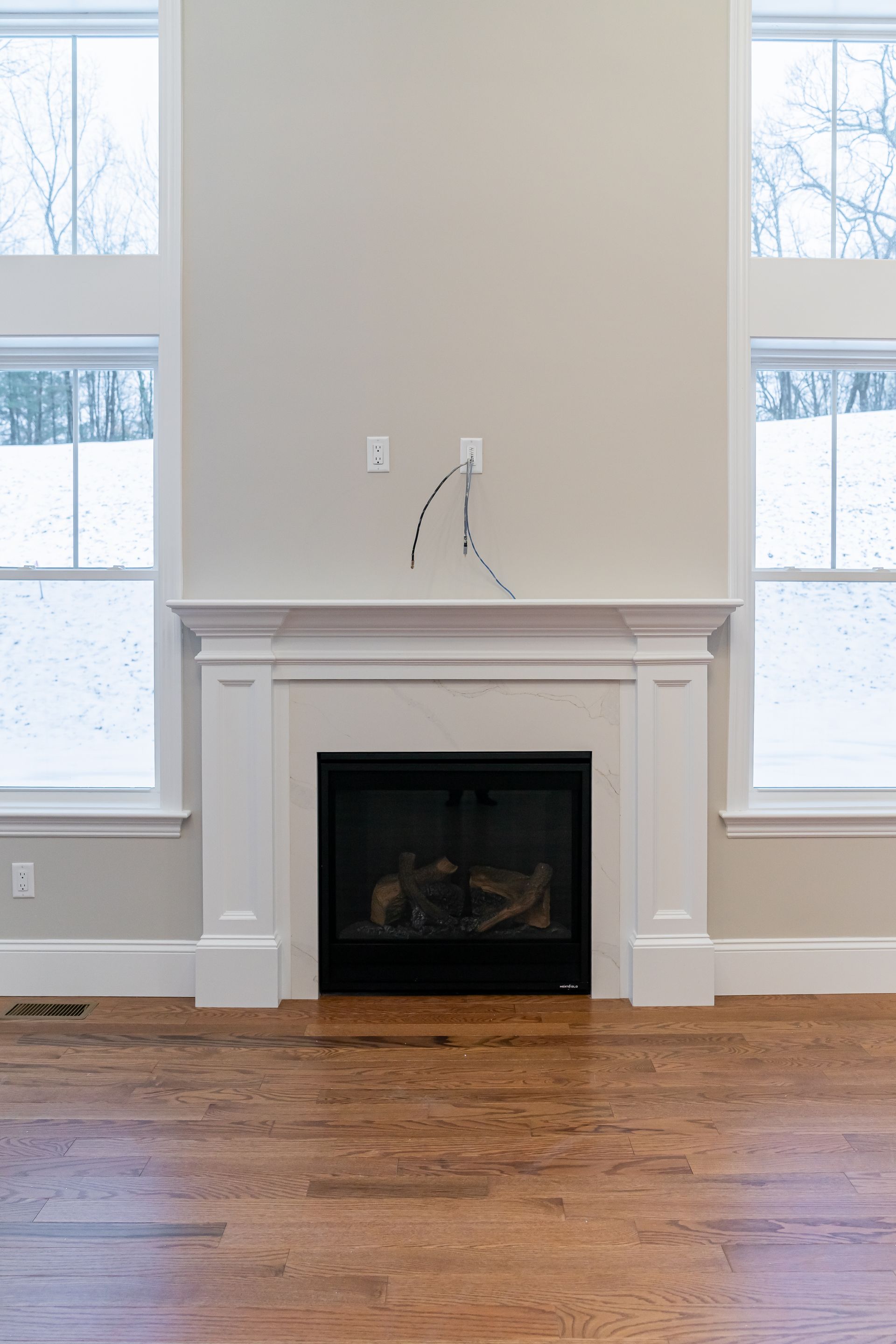 Empty living room with white fireplace, two tall windows, and hardwood floor