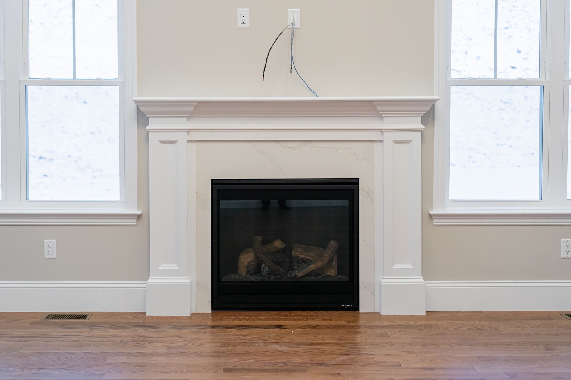 Empty living room with white fireplace, hardwood floor, and two windows