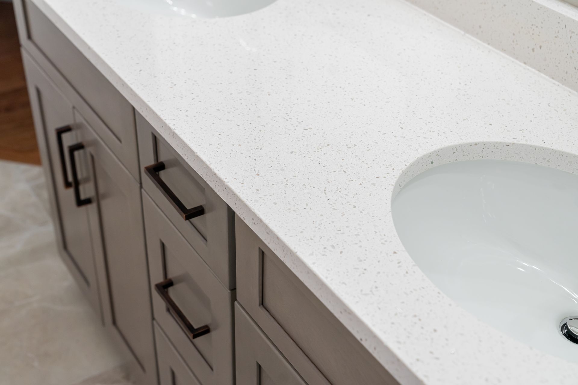 Bathroom vanity with white countertop, double sinks, and gray cabinets with black handles