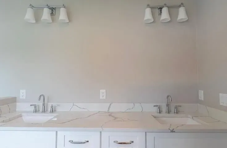 Double vanity bathroom with two sinks, white cabinets, and wall sconces above a beige countertop
