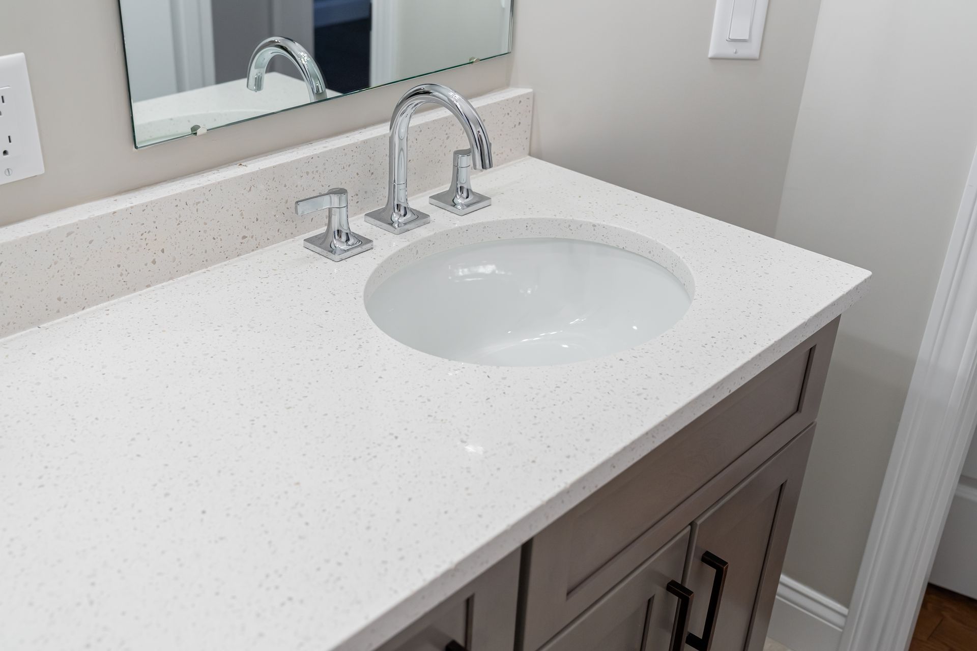White bathroom vanity with speckled countertop, oval sink, and chrome faucet under a mirror