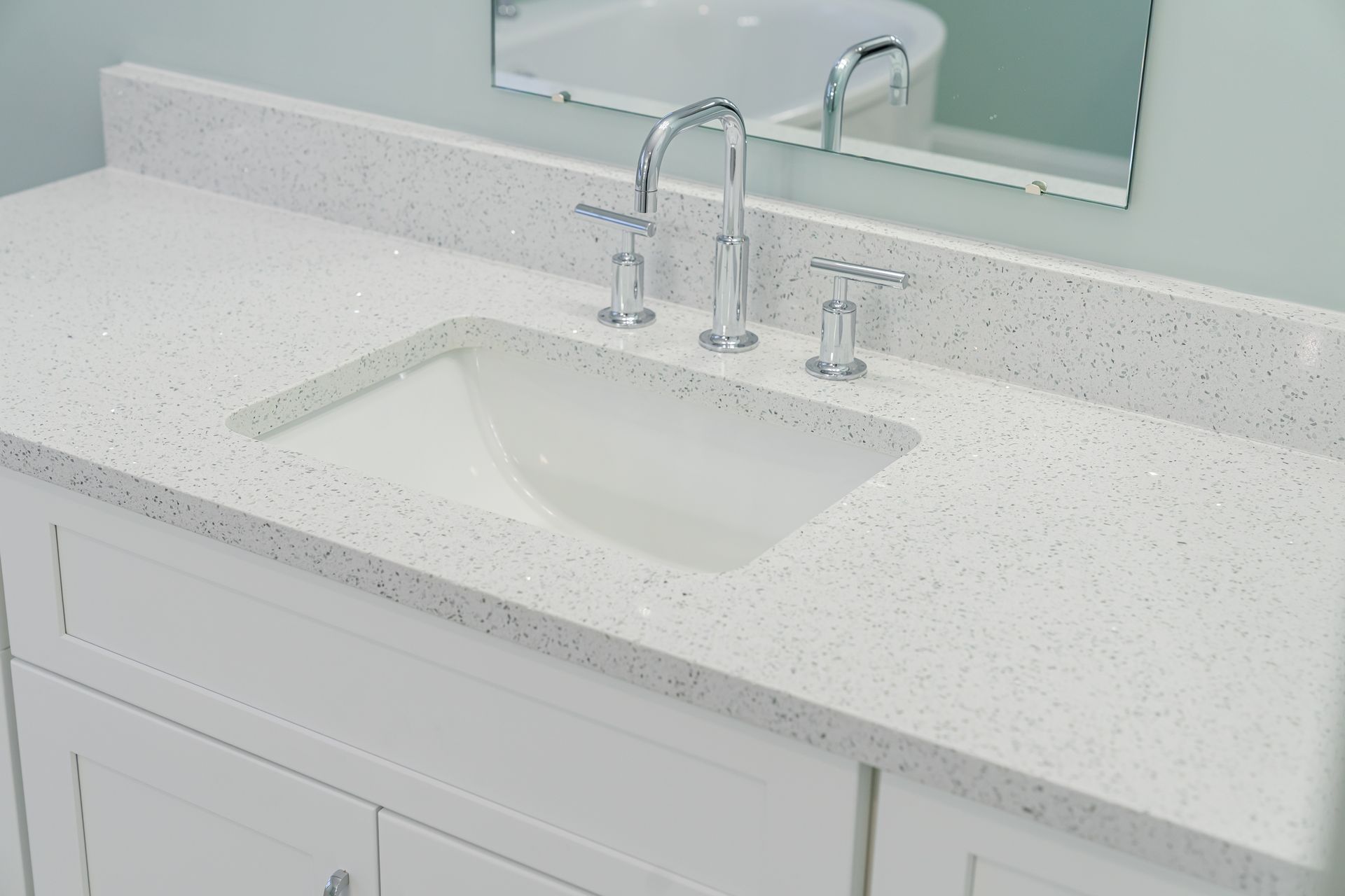 White bathroom vanity with speckled countertop, undermount sink, and chrome faucet