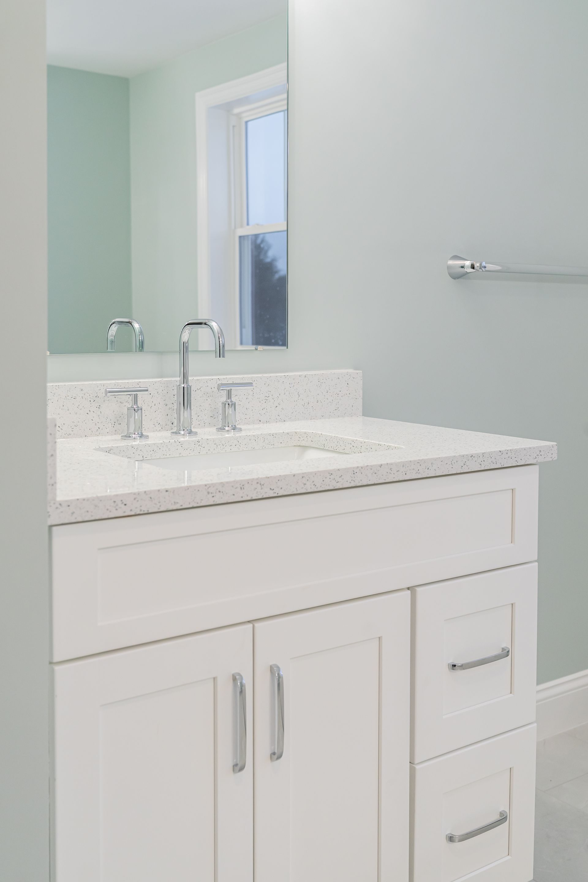 White bathroom vanity with marble countertop, mirror, sink, and chrome fixtures against pale blue walls